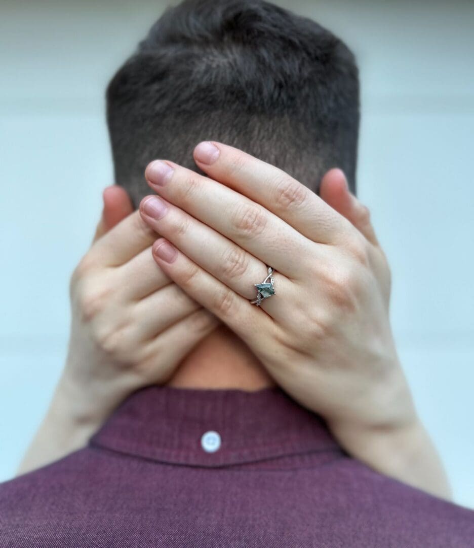 Hands with a ring embrace a man's neck from behind.