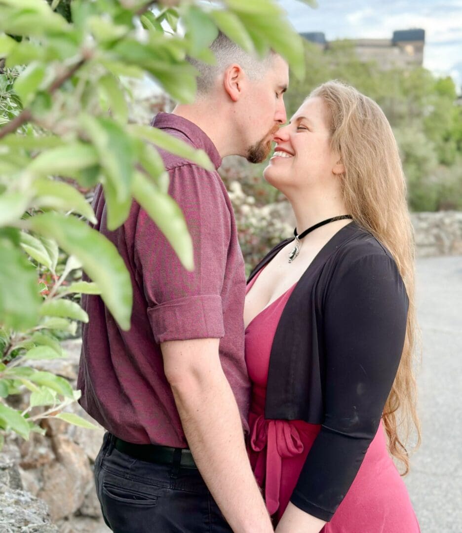 Couple sharing a tender kiss outdoors with greenery around.