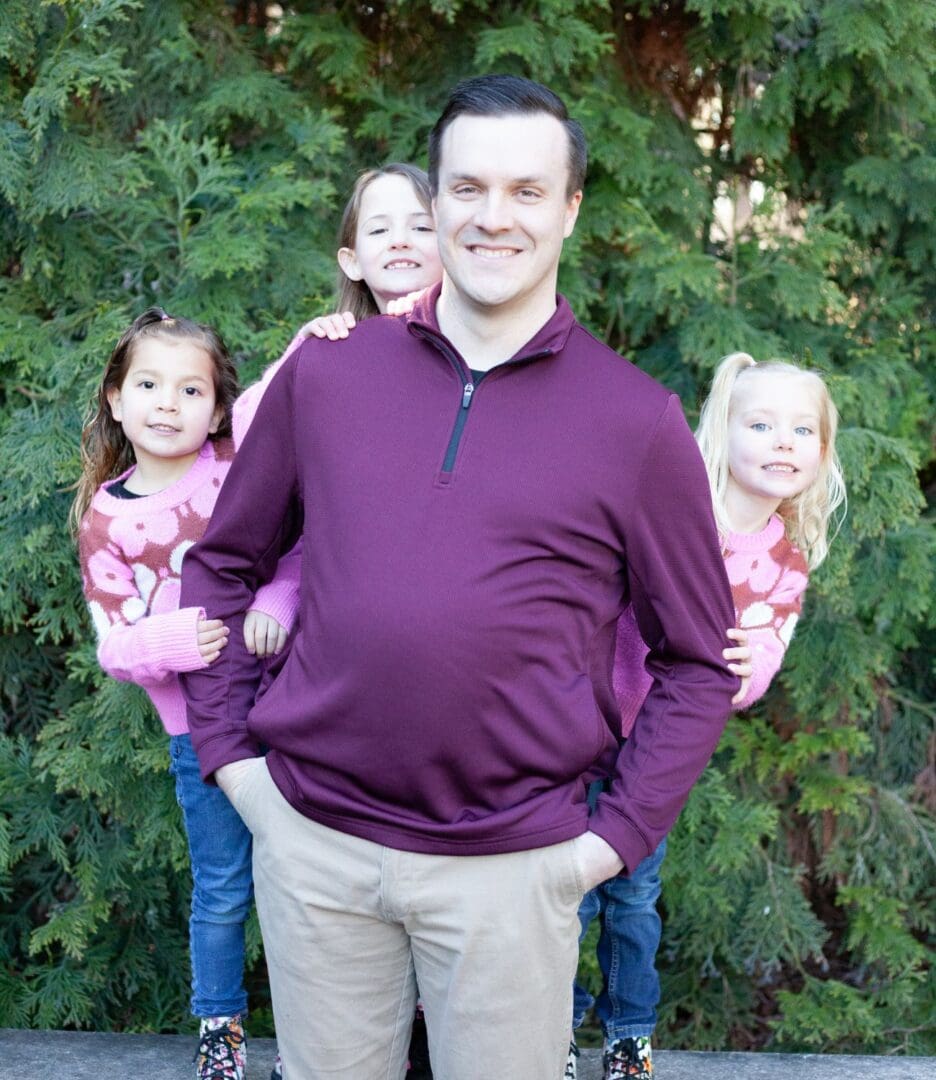 Man holding a baby with two young girls standing by his sides outdoors.