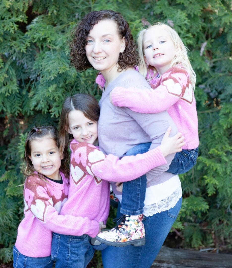 A joyful woman with three young girls in matching pink tops outdoors.