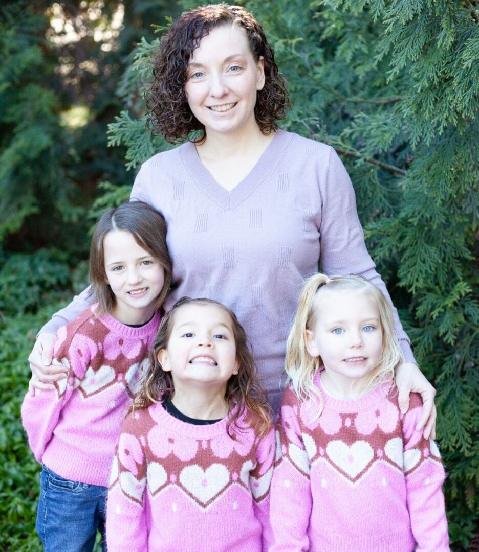 A smiling woman with three young girls wearing matching heart sweaters outdoors.