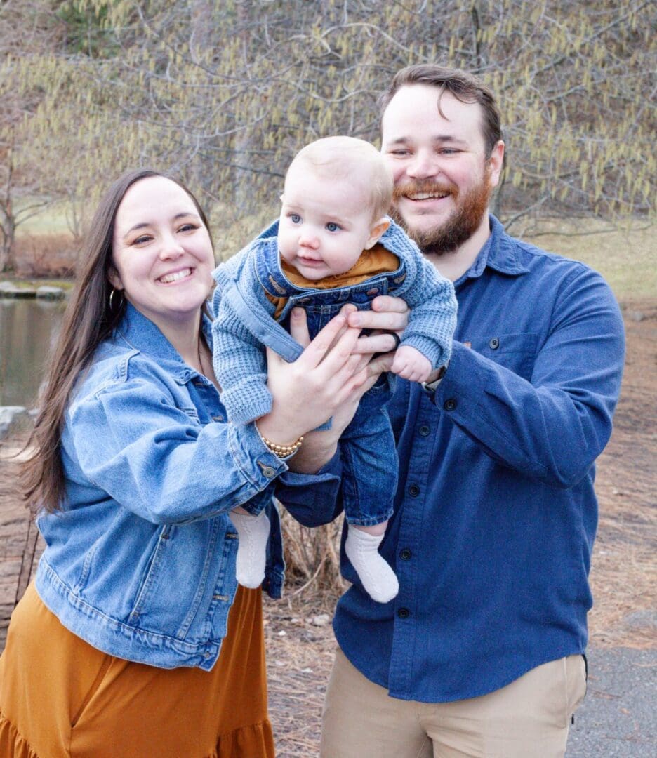 Smiling family of three outdoors, holding their baby.