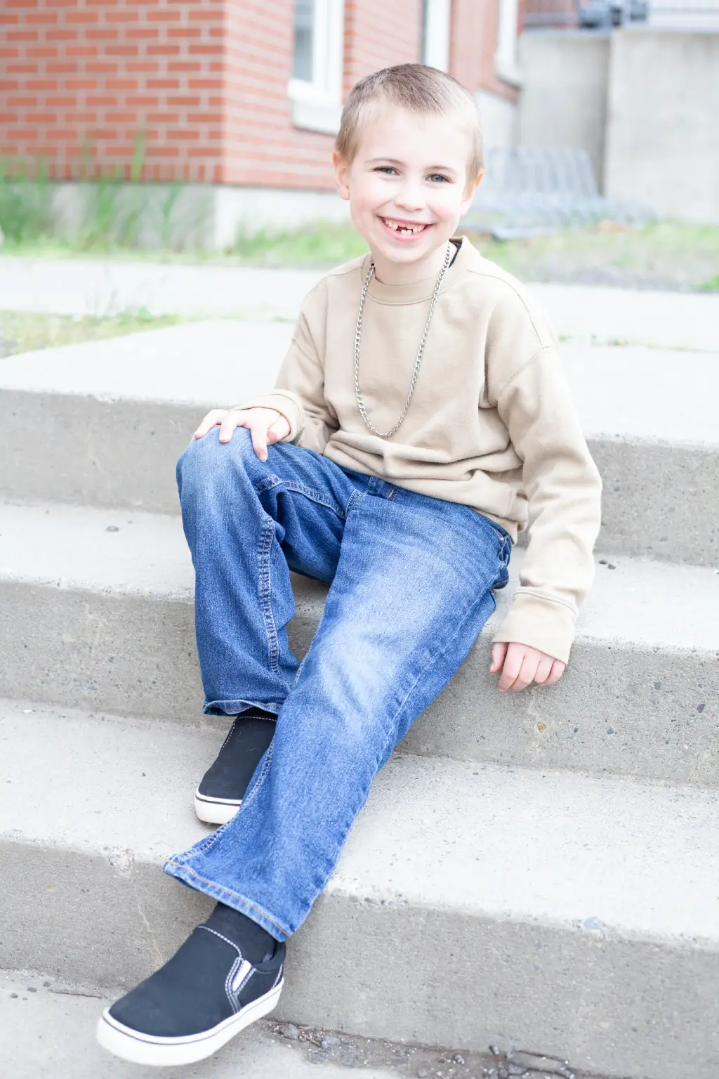 A smiling child sitting on outdoor steps wearing a beige top and blue jeans.