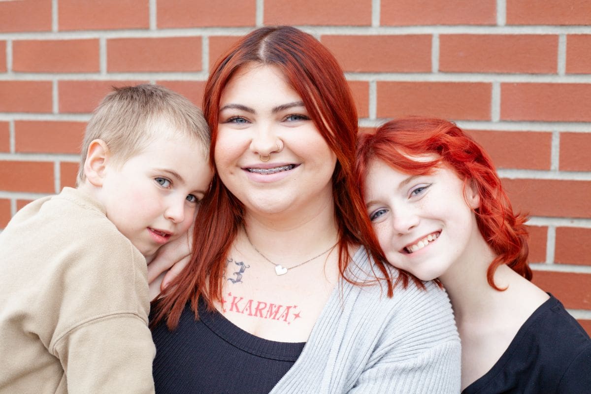 Three friends smiling warmly in front of a brick wall.