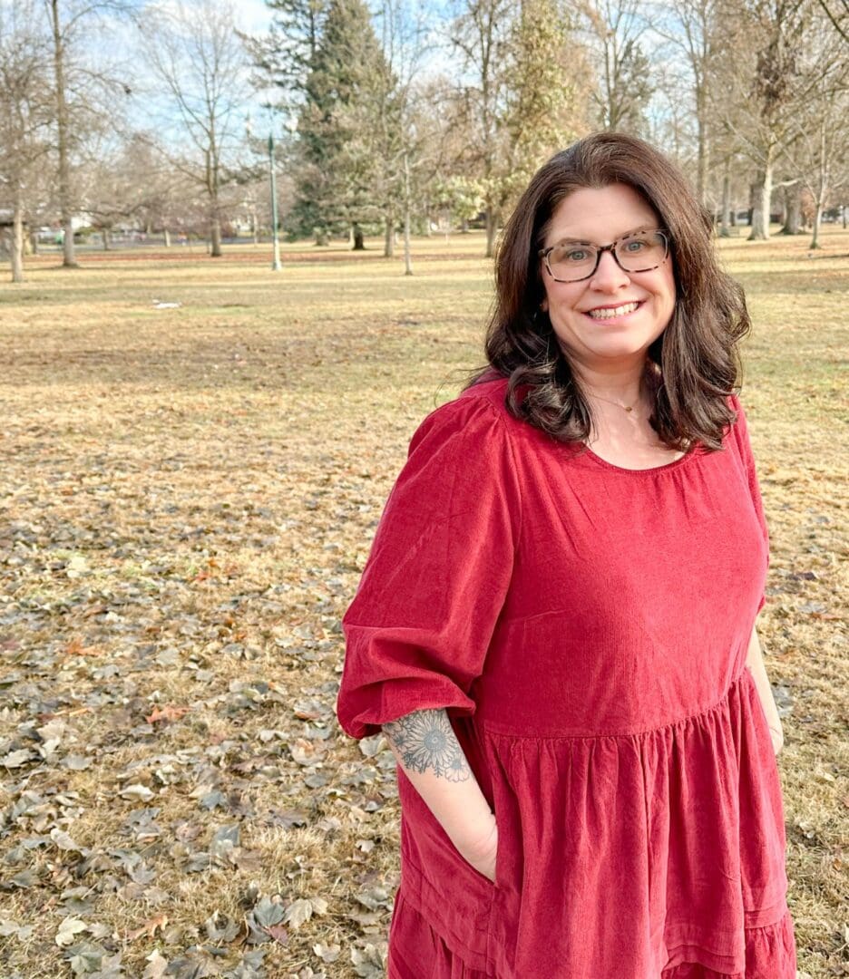 Woman in a red dress standing outdoors with a smile.