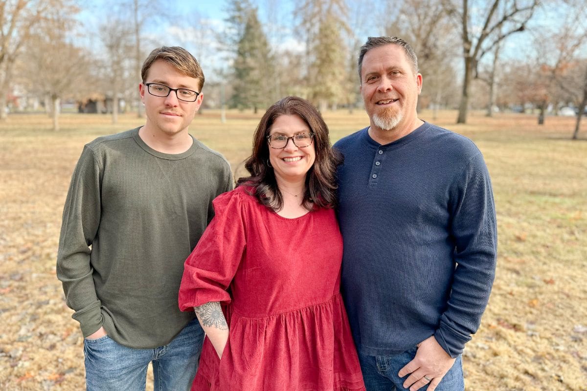 A smiling family of three posing outdoors on a sunny day.