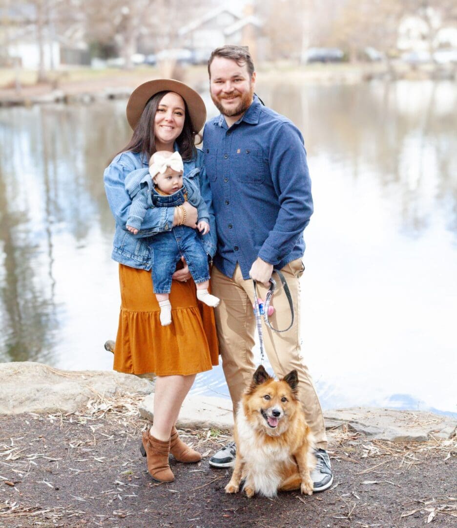 A happy couple with their two dogs near a lake on a chilly day.
