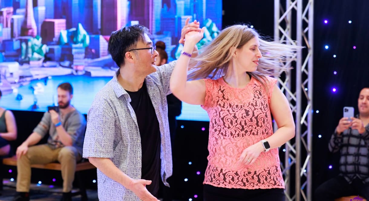 A couple dancing joyfully together at an event with colorful lights.