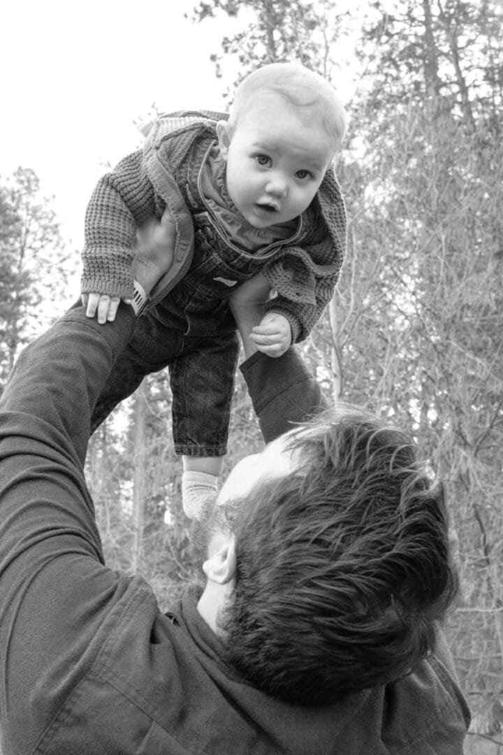 A joyful moment of a father lifting his baby in the air outdoors.