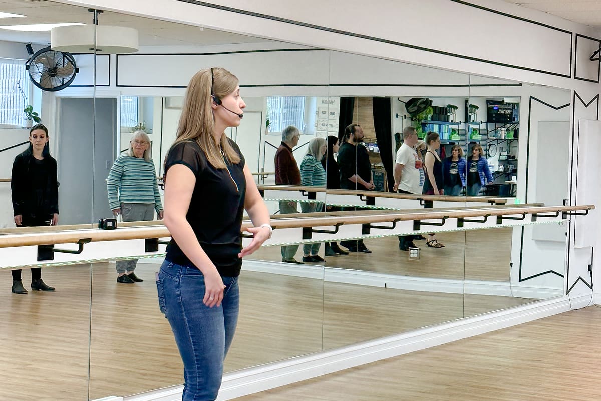A woman wearing a mask looking thoughtfully at her reflection in a large mirror.