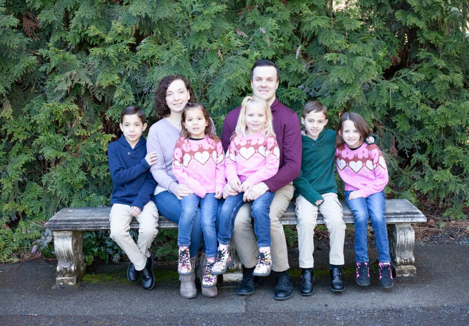 A family of six sitting together outdoors in front of greenery.
