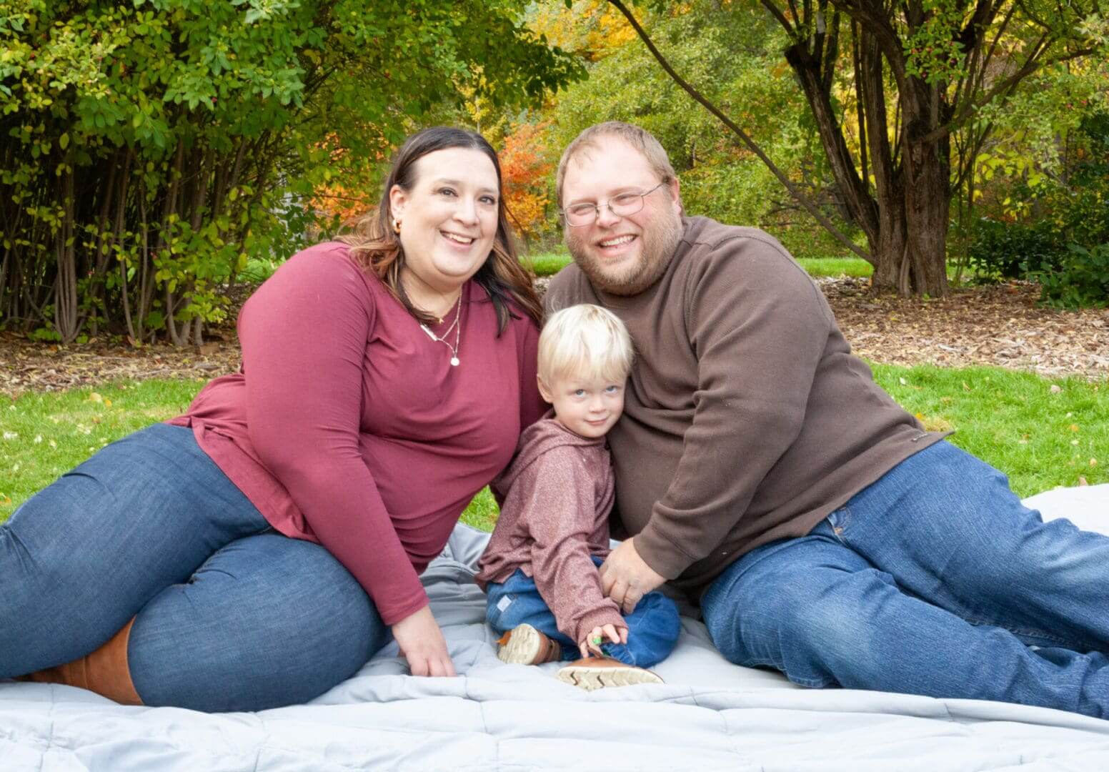 Family sitting on blanket outdoors, smiling.