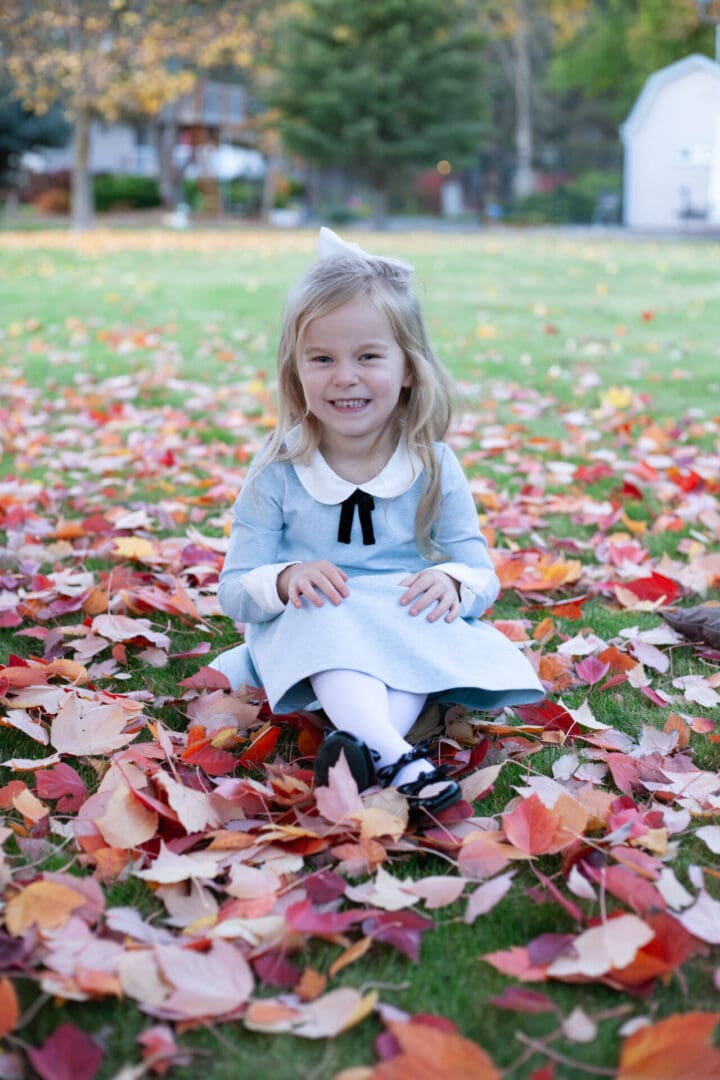 Girl sitting on grass with autumn leaves.