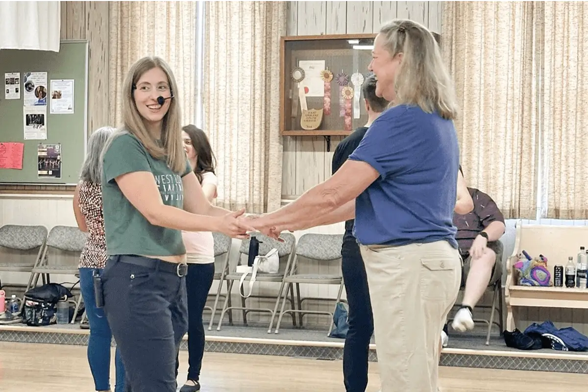 Two women holding hands and smiling indoors during a social event