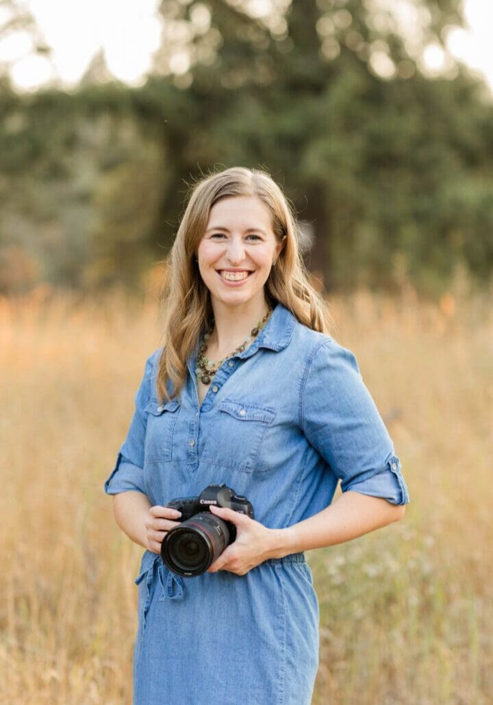 Woman smiling, holding camera in field.