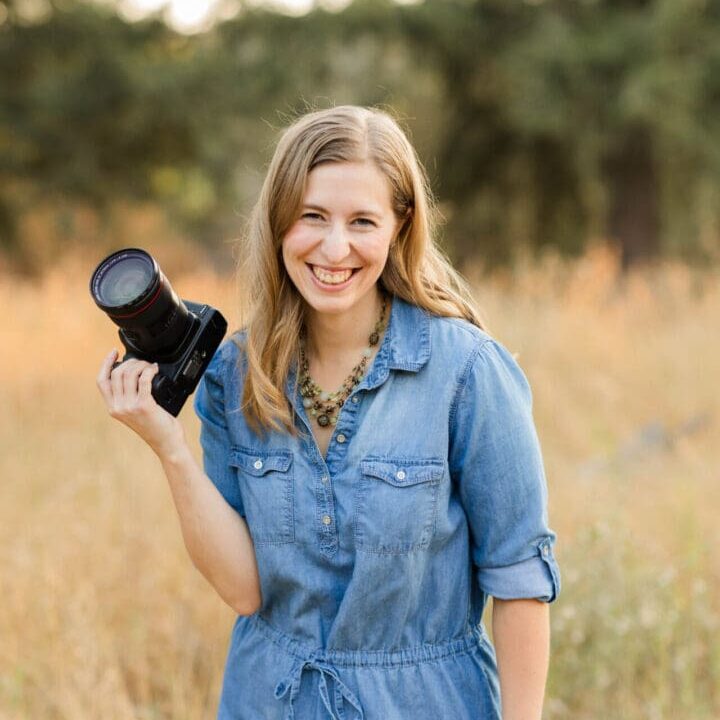 Smiling woman holding camera in field.